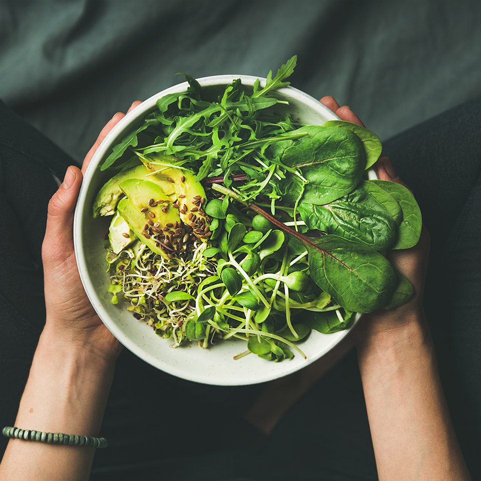 Raw food breakfast meal in bowl with spinach, arugula, avocado, seeds and sprouts