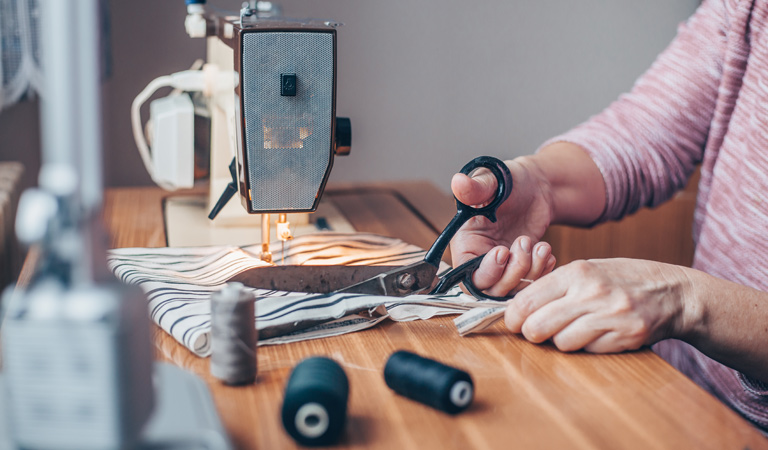 A woman learning how to sew cutting fabric at her sewing kit.