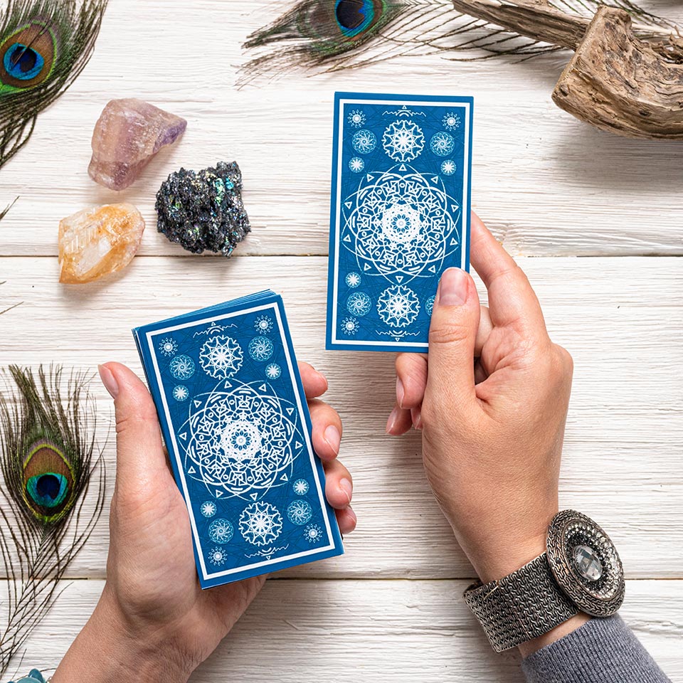 Fortune teller holding blue oracle cards above a white wooden table.