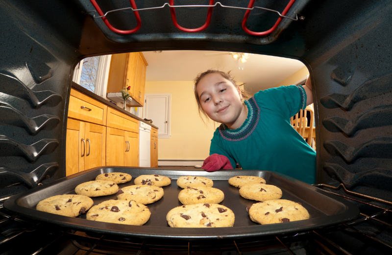 girl taking tray of cookies out of the oven