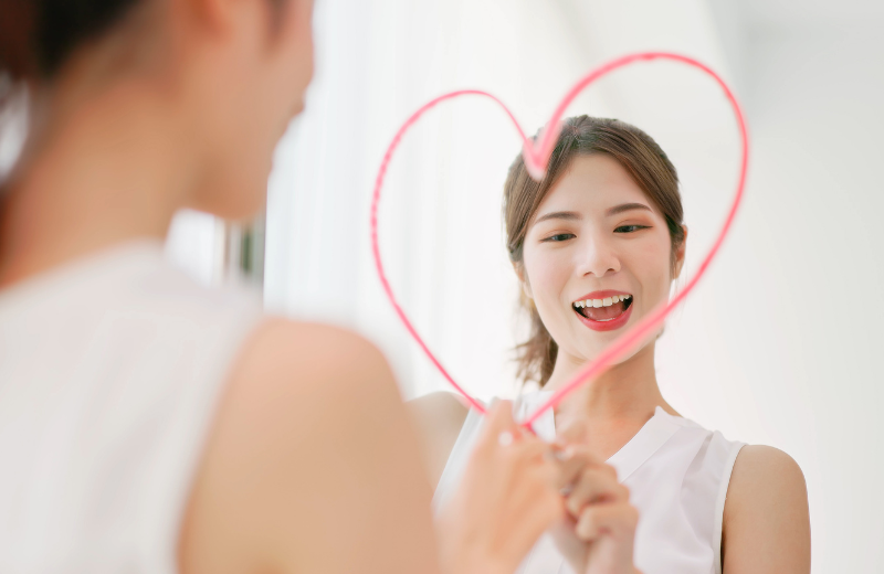 smiling woman drawing a love heart on the mirror