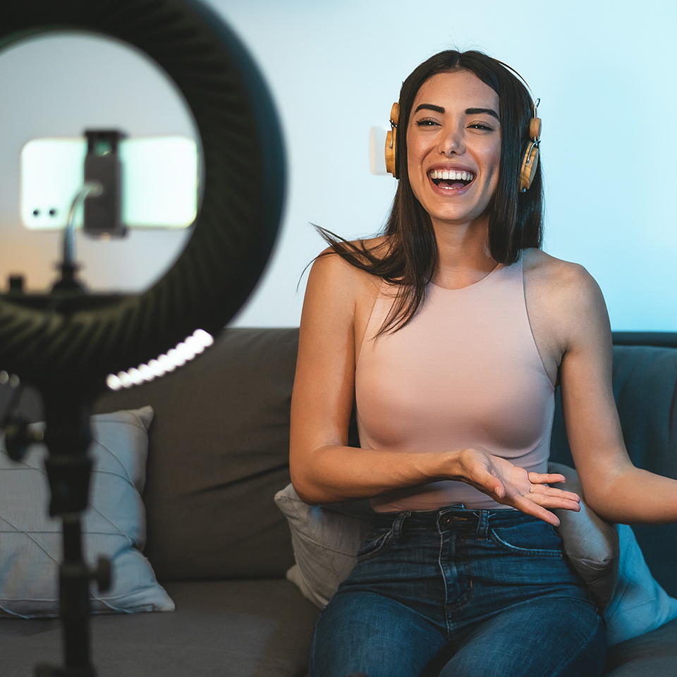 Female influencer vlogging online with smartphone camera and laptop
