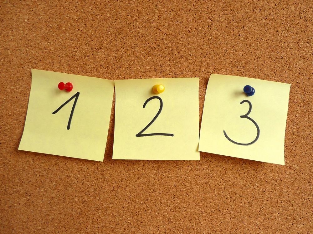 The numbers 1, 2 and 3 written on separate sticky notes and attached to a clipboard