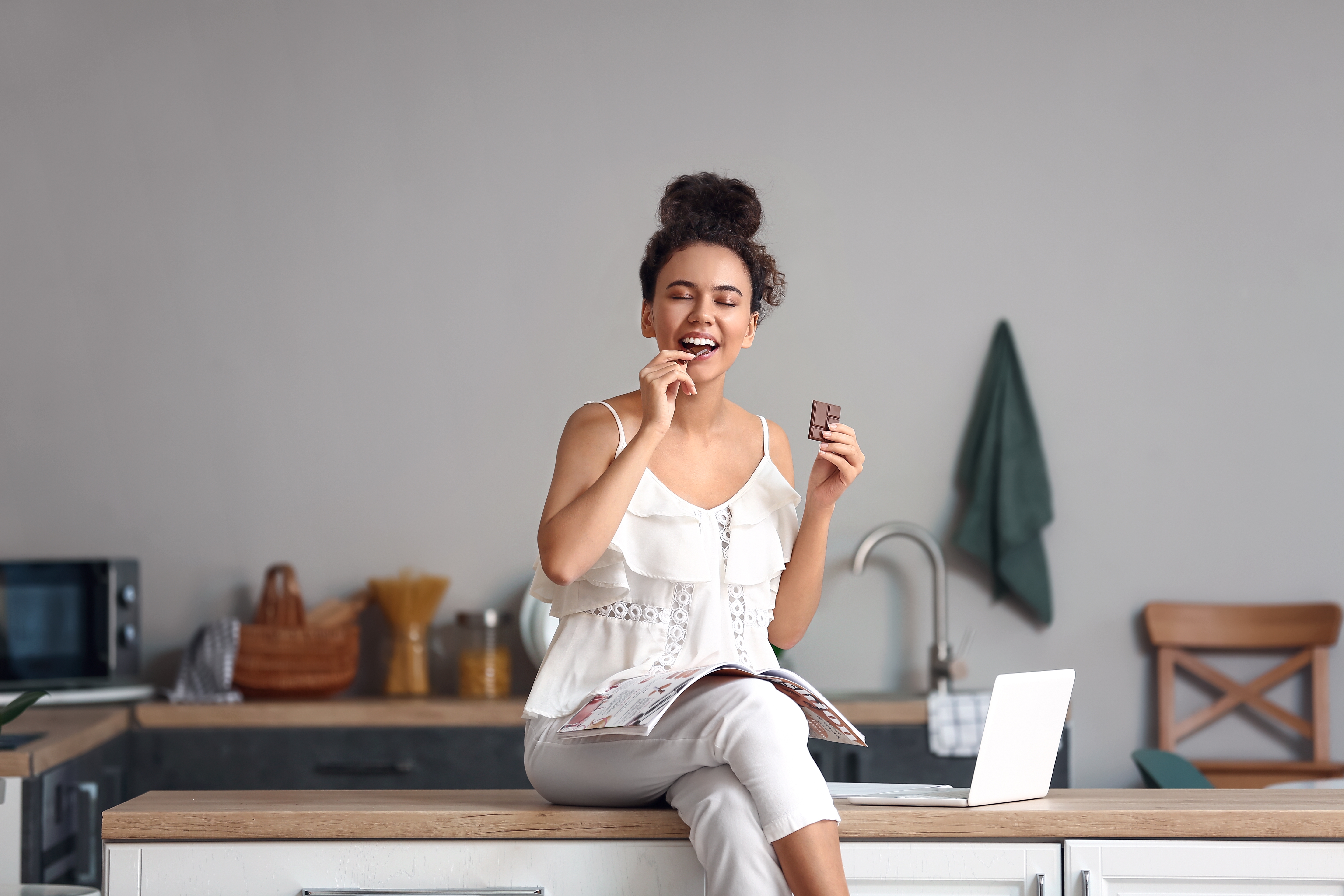 Happy woman eating chocolate in the kitchen as a reward