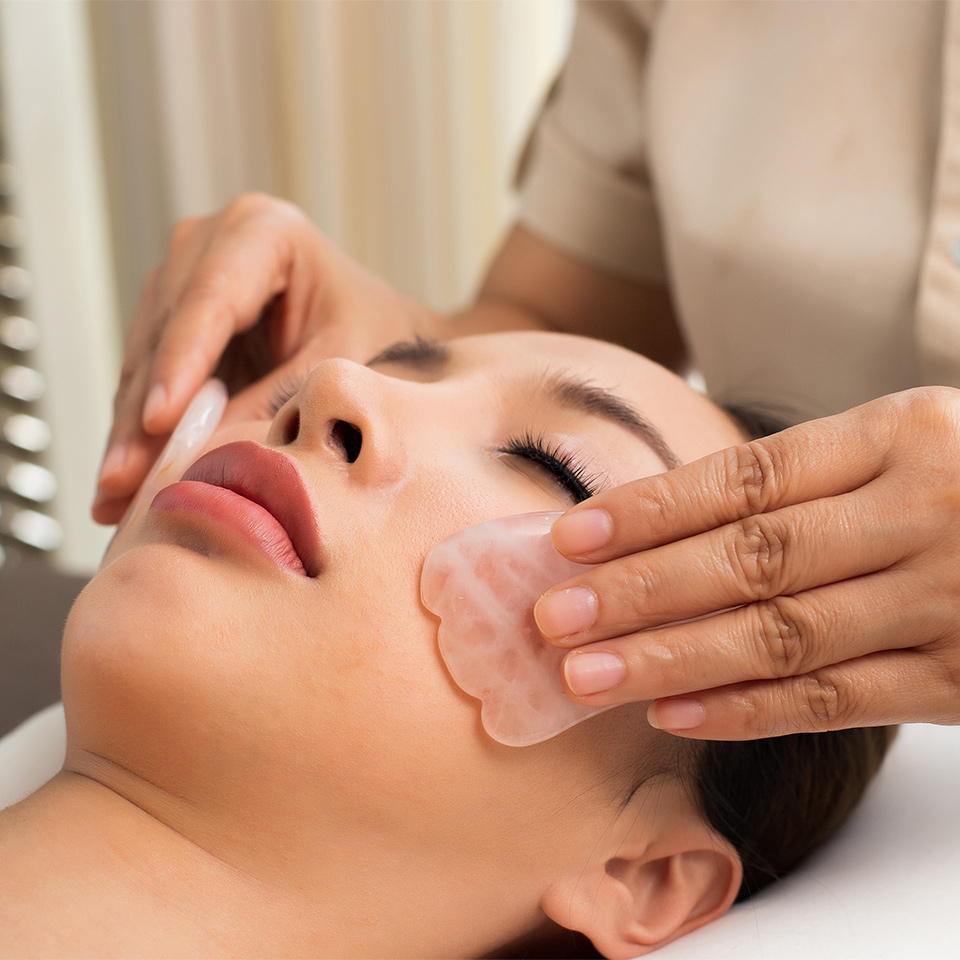 Reflexologist using Gua Sha massage tools on a woman's face