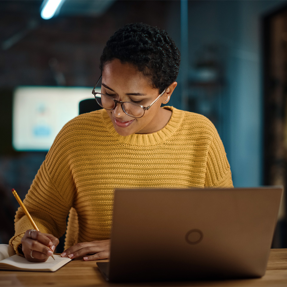 Person making handwritten notes as they work at a laptop