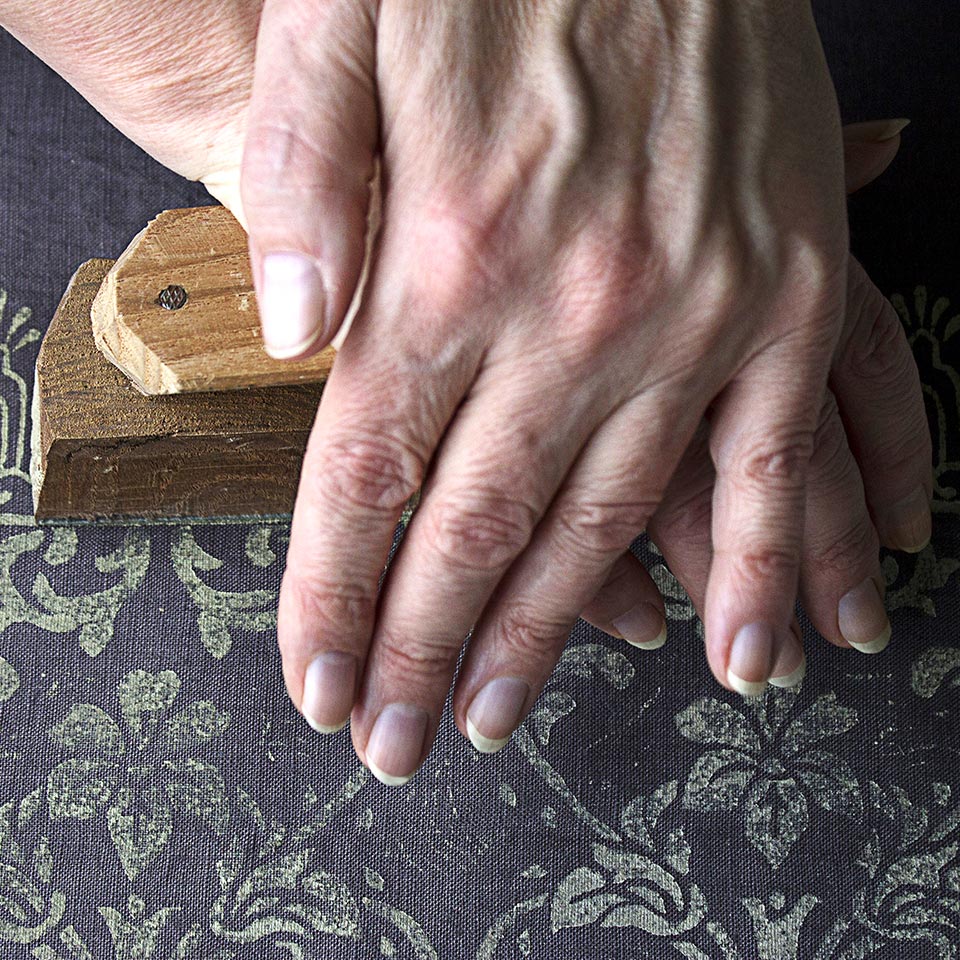 A pair of hands pressing down on a printing block to make a pattern on a piece of textile