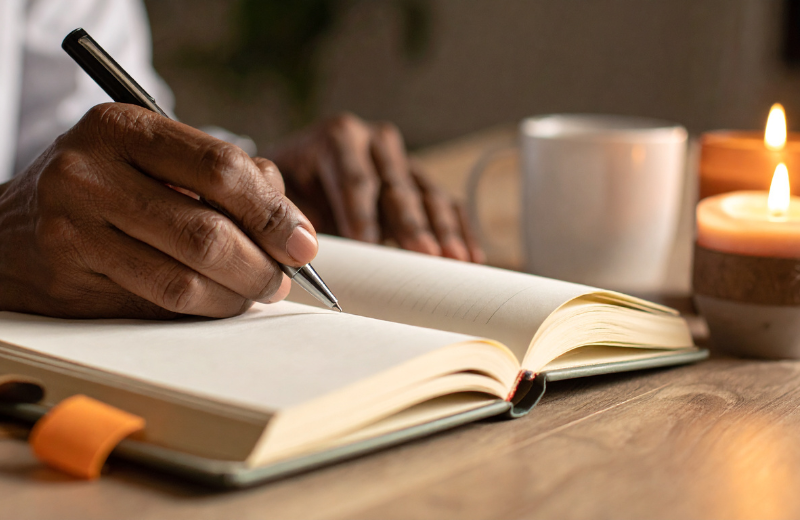someone writing in a journal with a candle