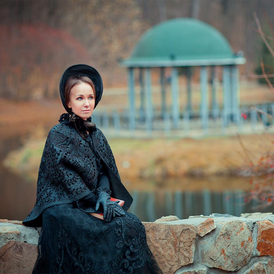 Woman in a long black dress and hood sitting on a stone wall
