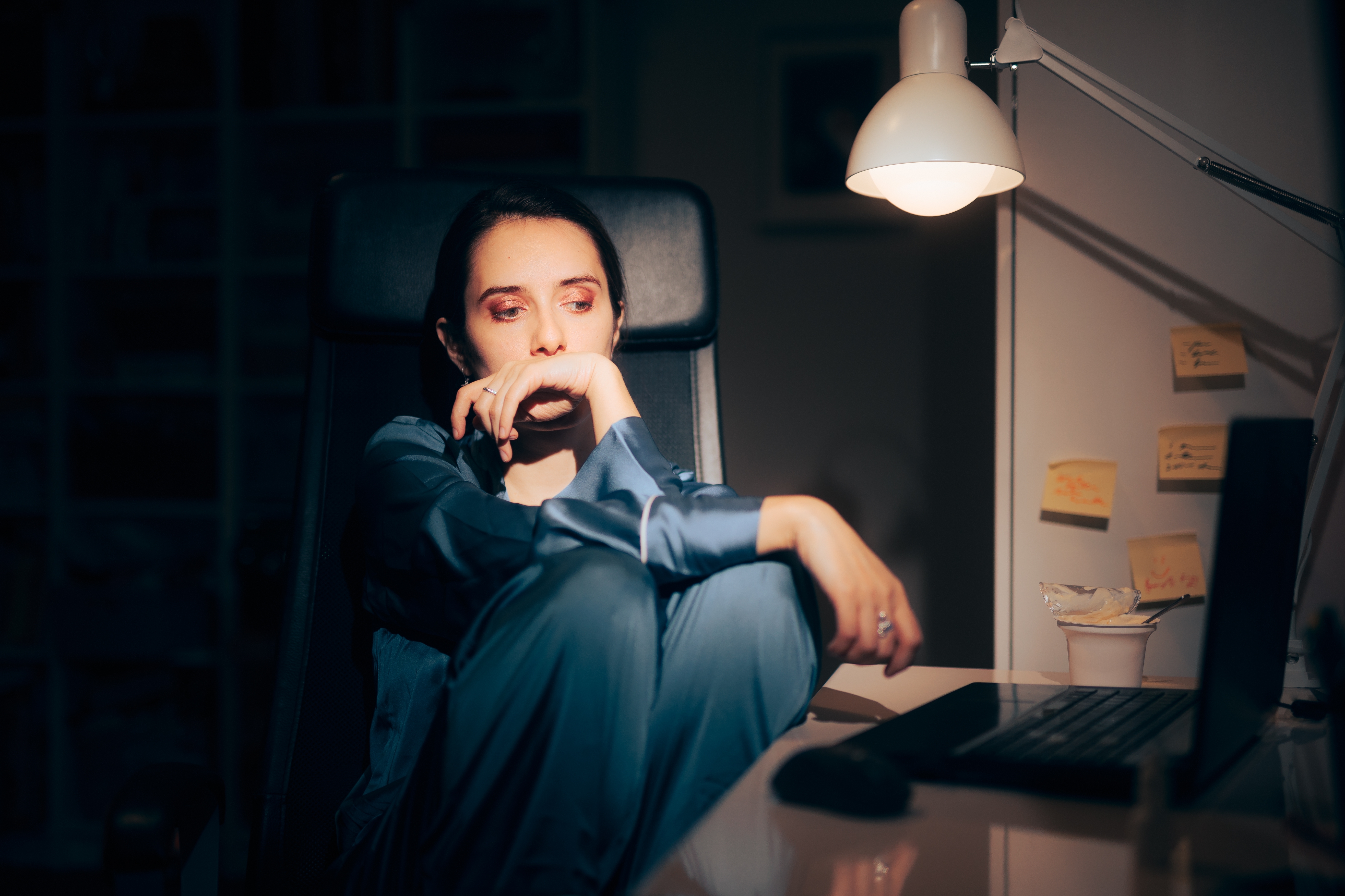 Someone sat at a desk in a dark room, looking sad