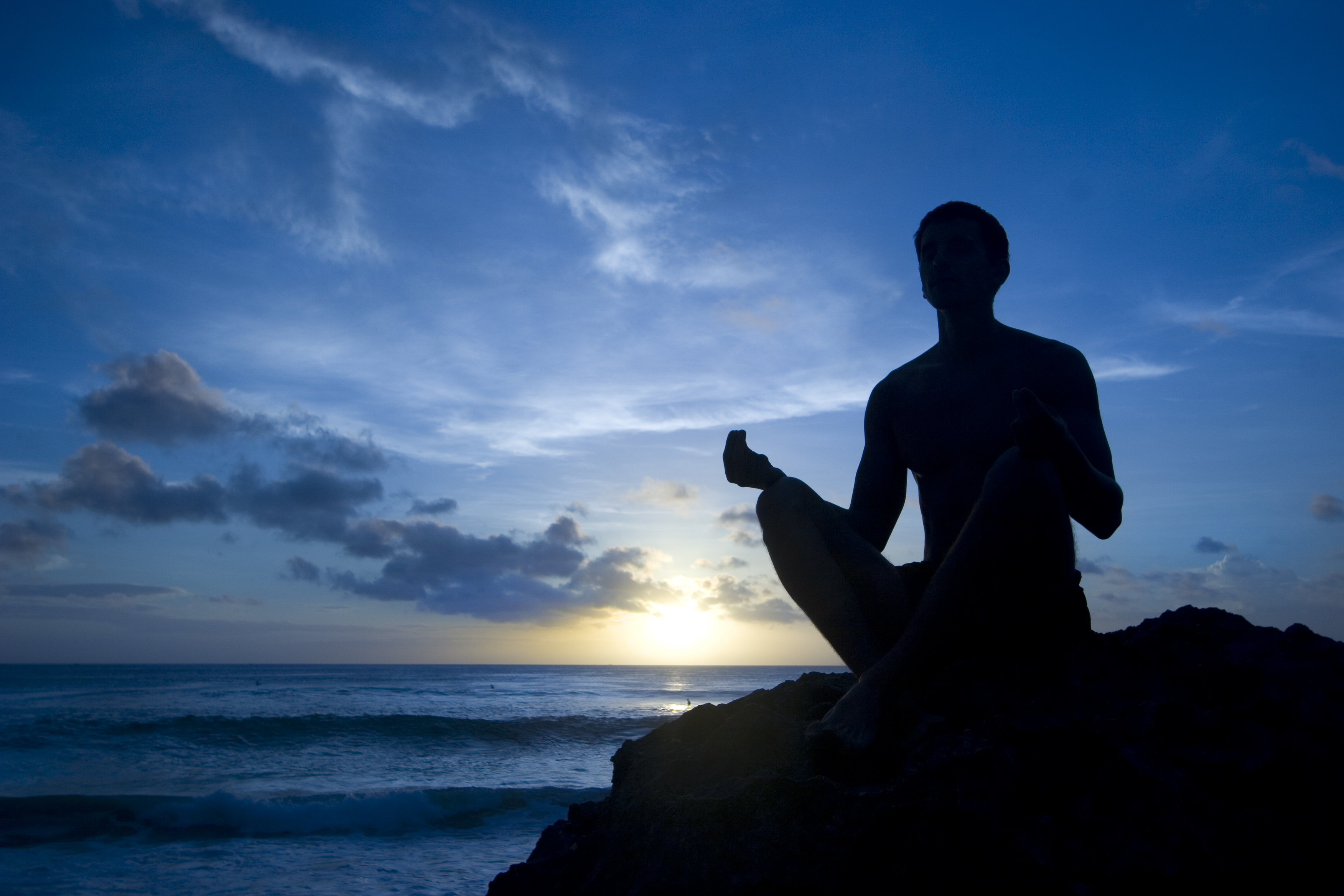 Silhouette of someone meditating next to the sea at sunrise