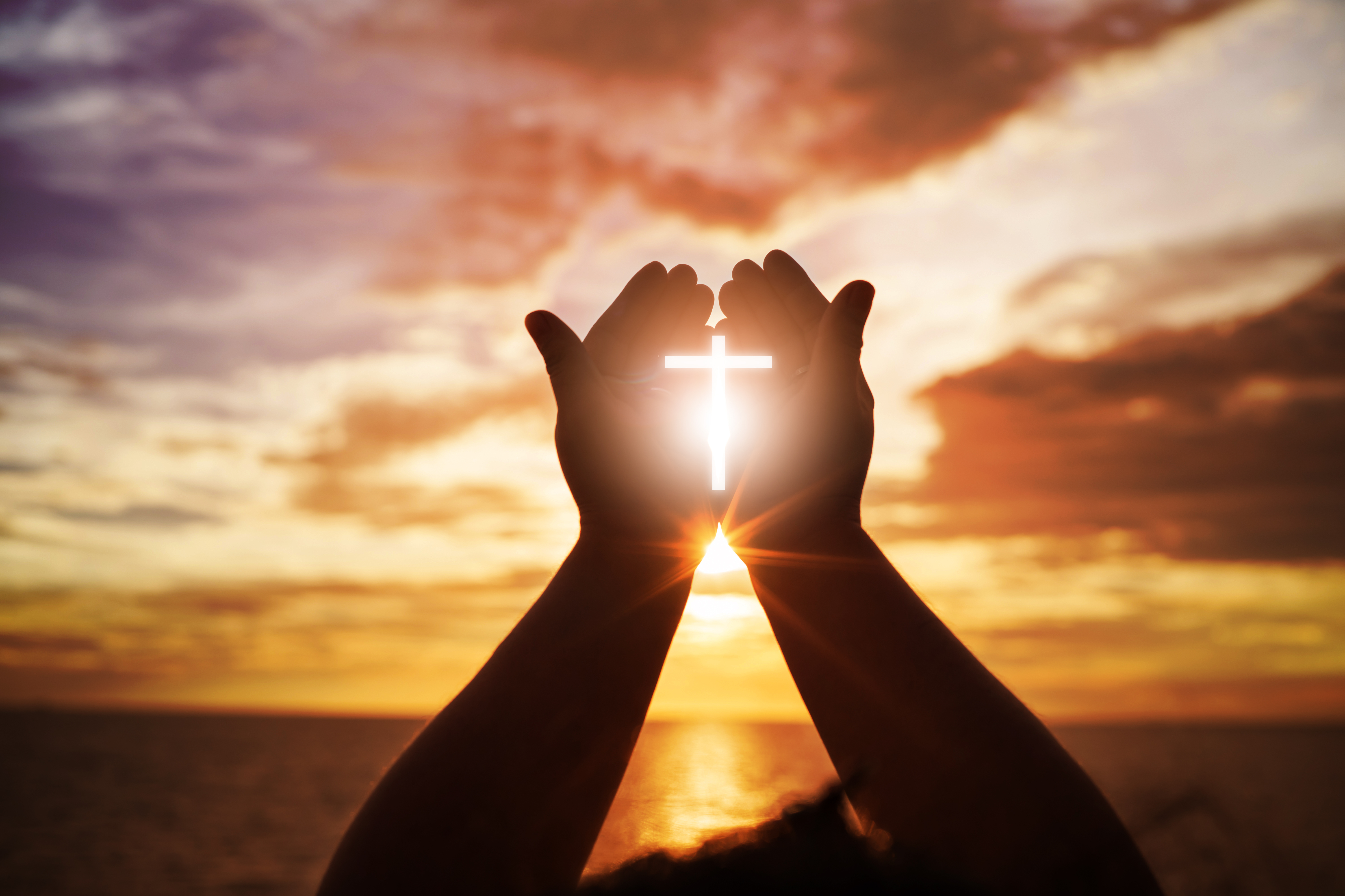 Christianity cross in someone's hands at sunset