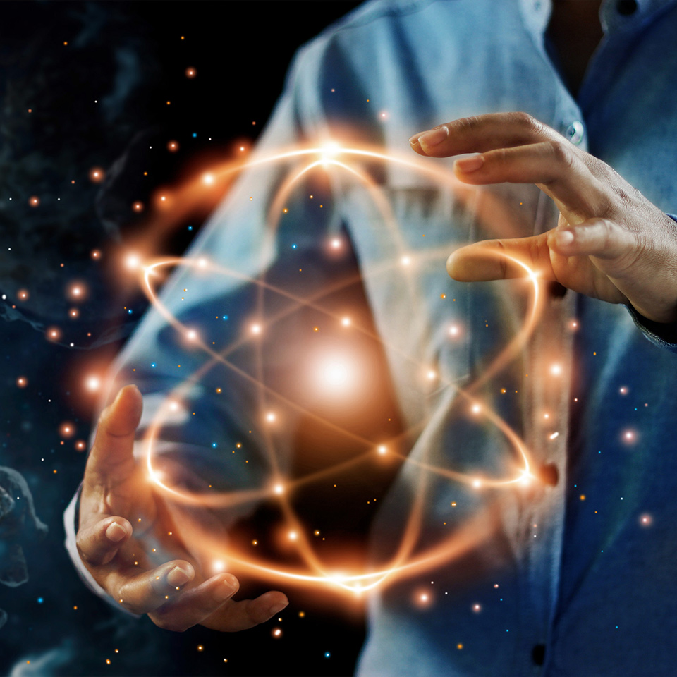 Hands holding an enlarged atomic particle with a space background.