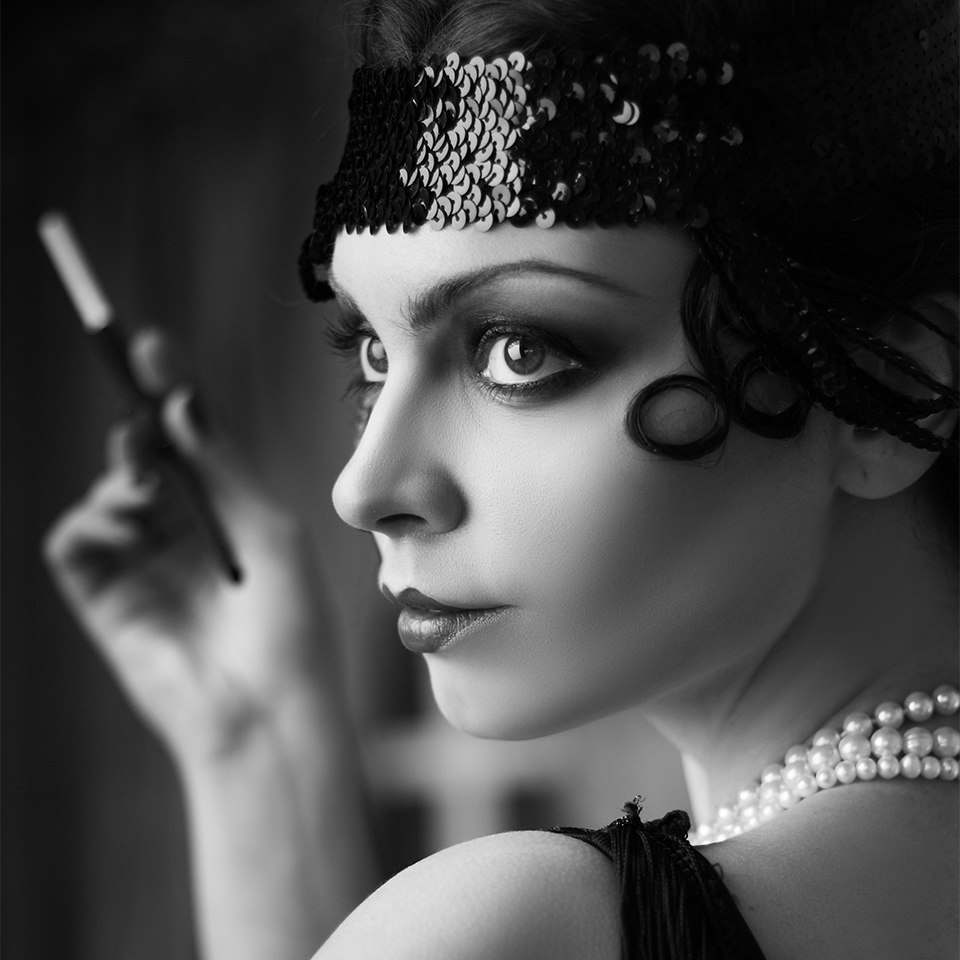 A black and white, close up portrait of a woman wearing a flapper style headband