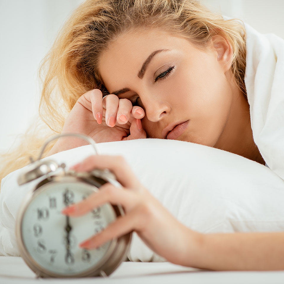 Woman in bed, looking tired, turning alarm clock off