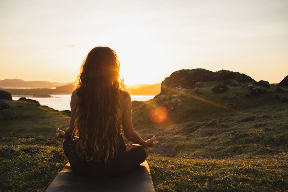 Woman sat outside meditating in front of a sunrise
