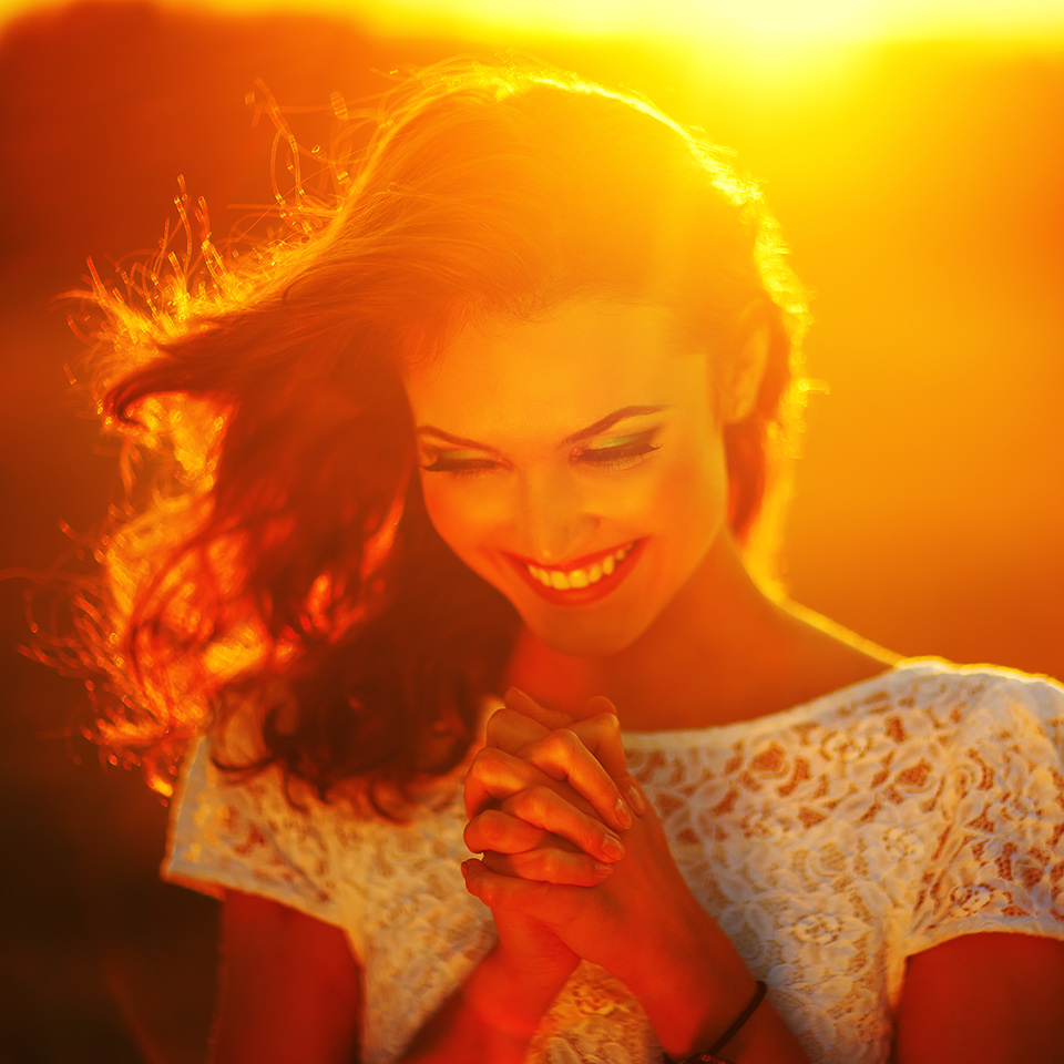 A young girl praying while the sun sets behind her