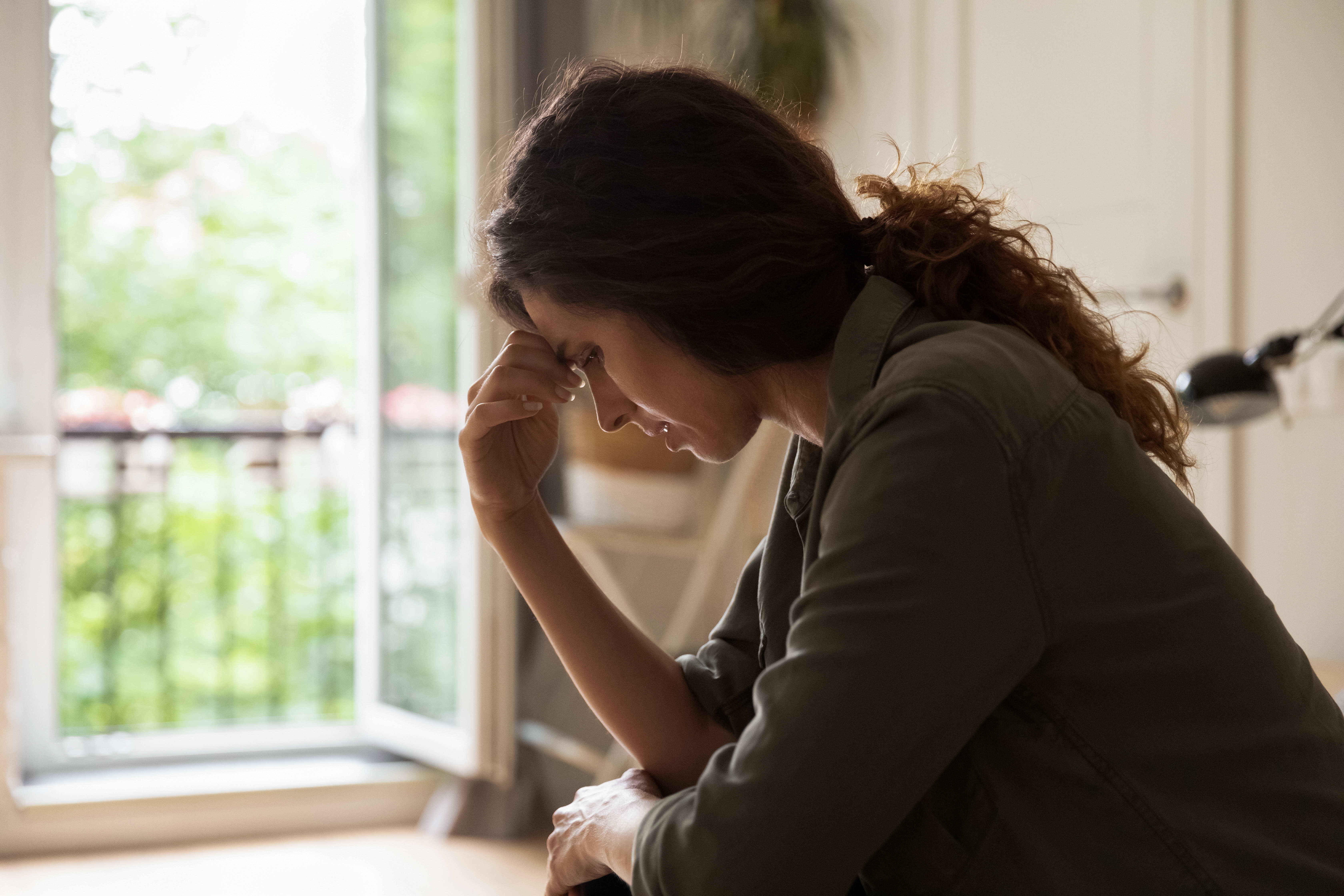 A woman sitting down with her head bowed and her hand against her forehead