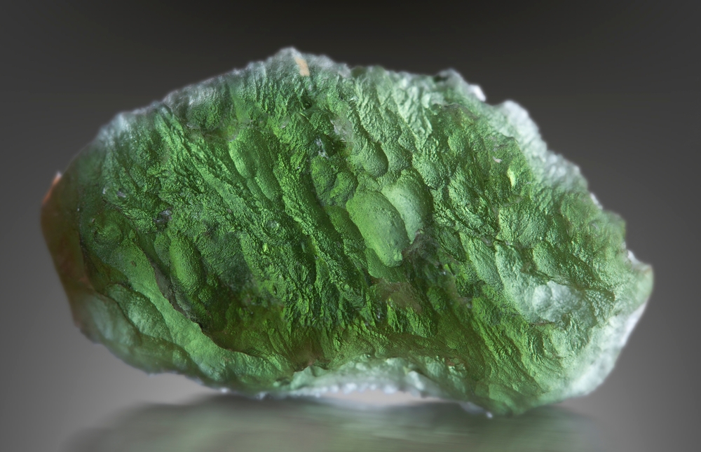 A piece of Moldavite on a grey background