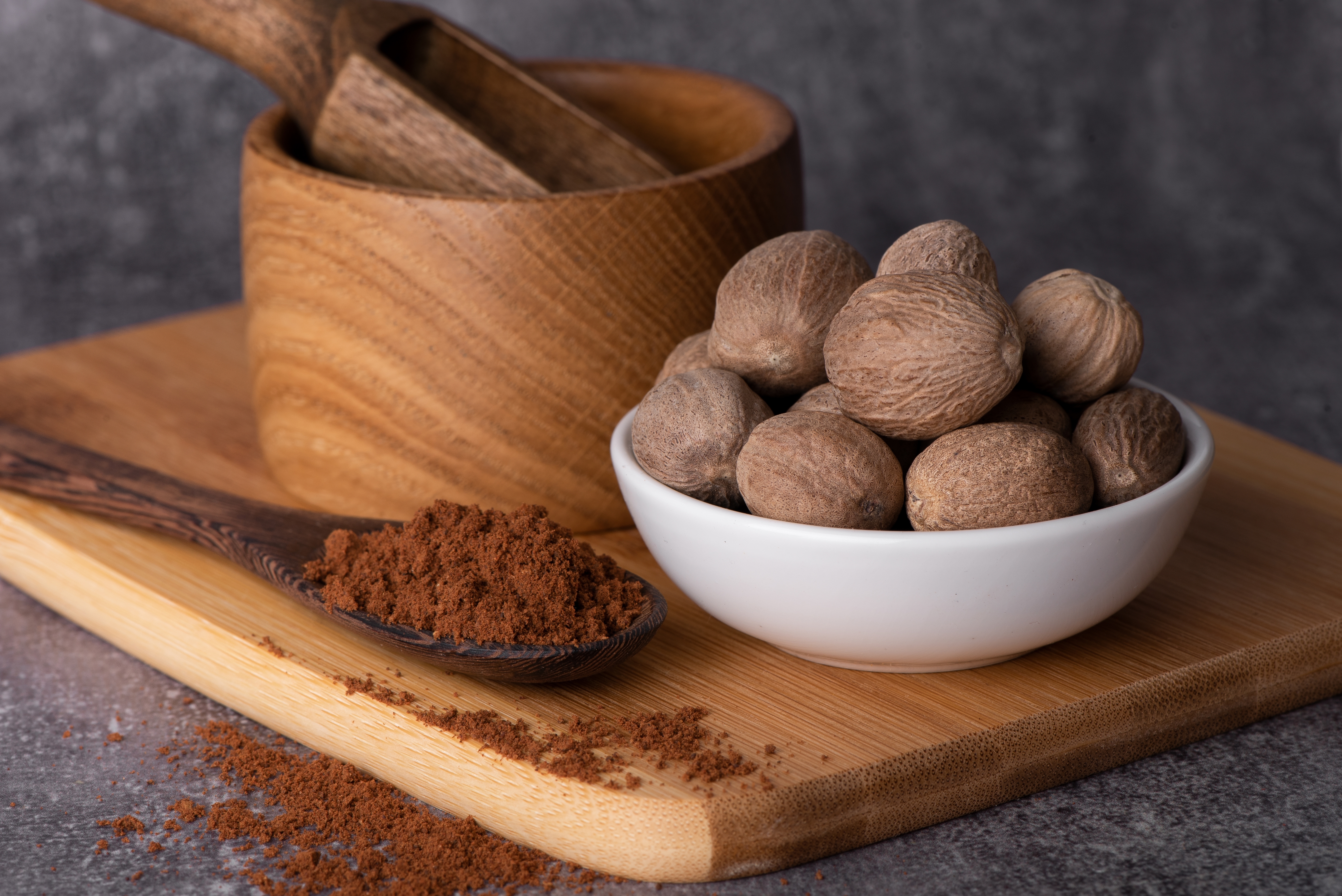 Whole nutmeg in a bowl beside ground nutmeg