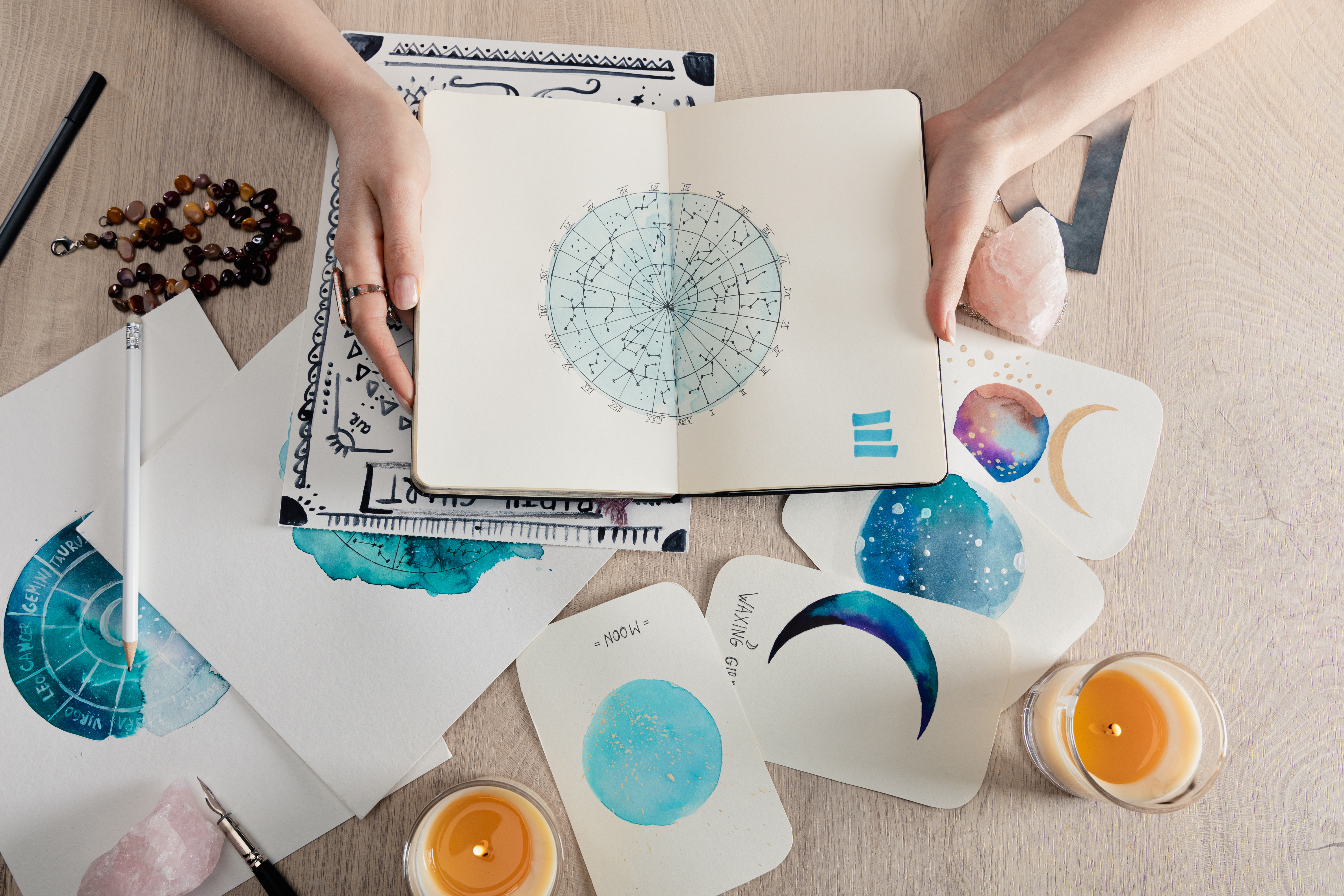 A zodiac wheel in a notebook with numerous candles and cards surrounding it, including one with an image of a moon