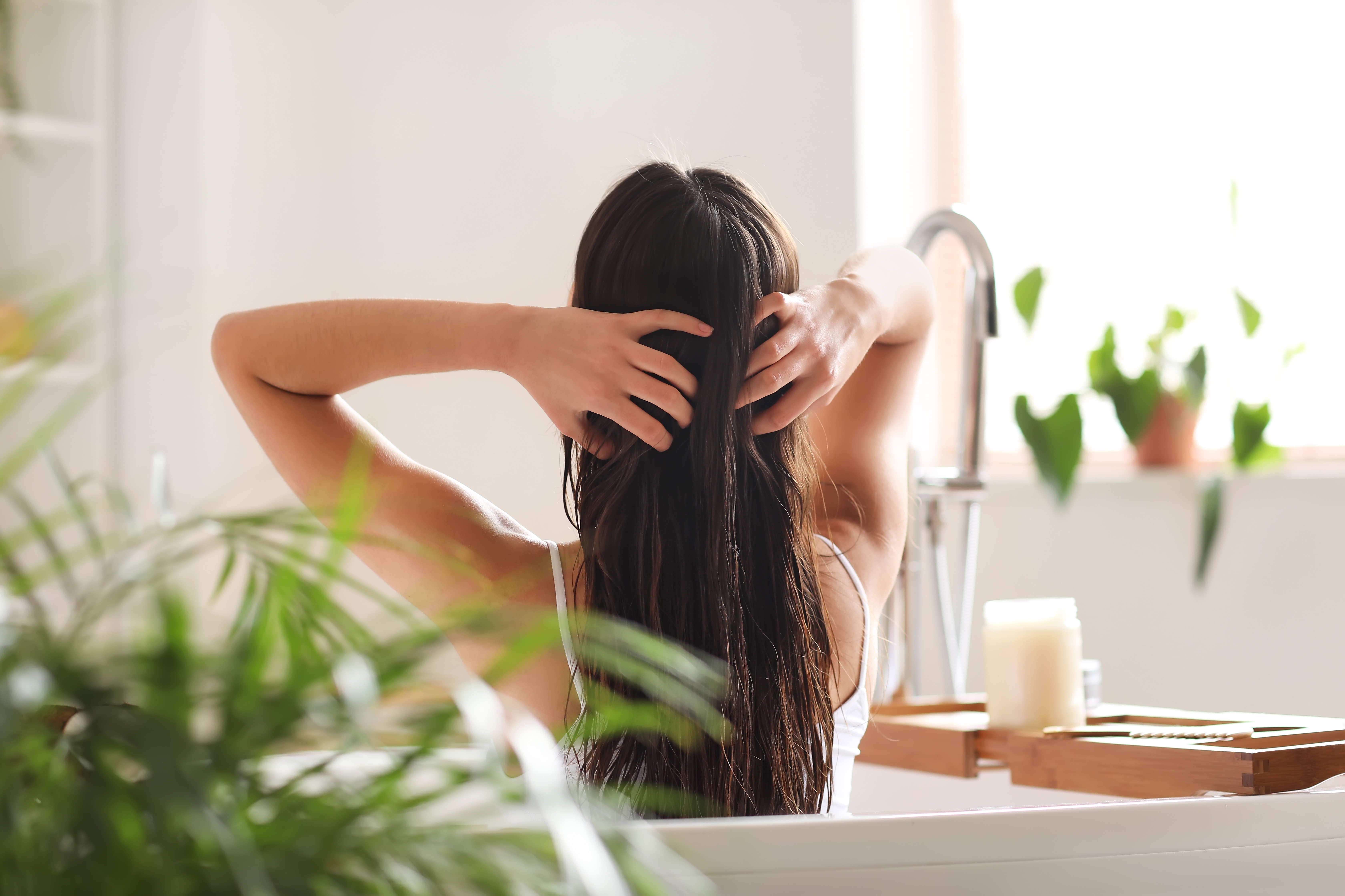 A woman in the bath applying a mask to her hair