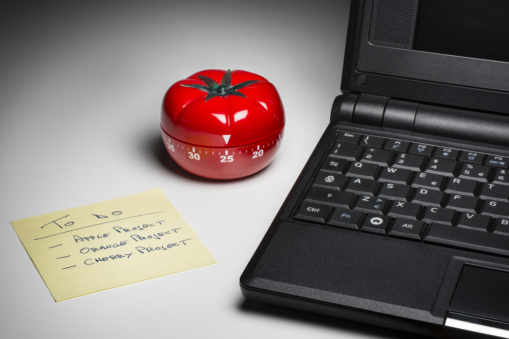 A tomato shaped timer next to a laptop and a to do list