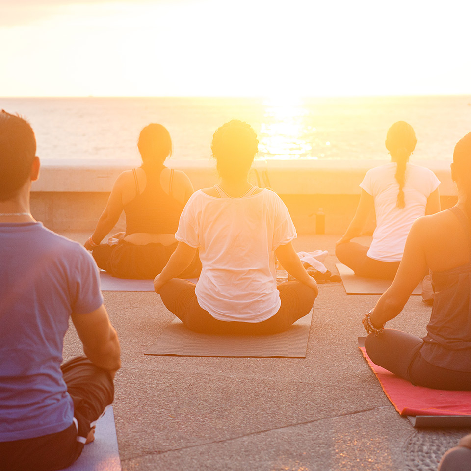 Group of people sitting and meditating outside at sunset