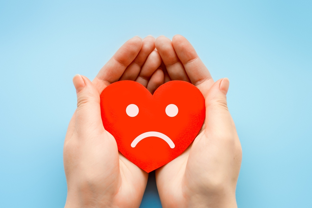 Hands holding a red love heart with a sad face on