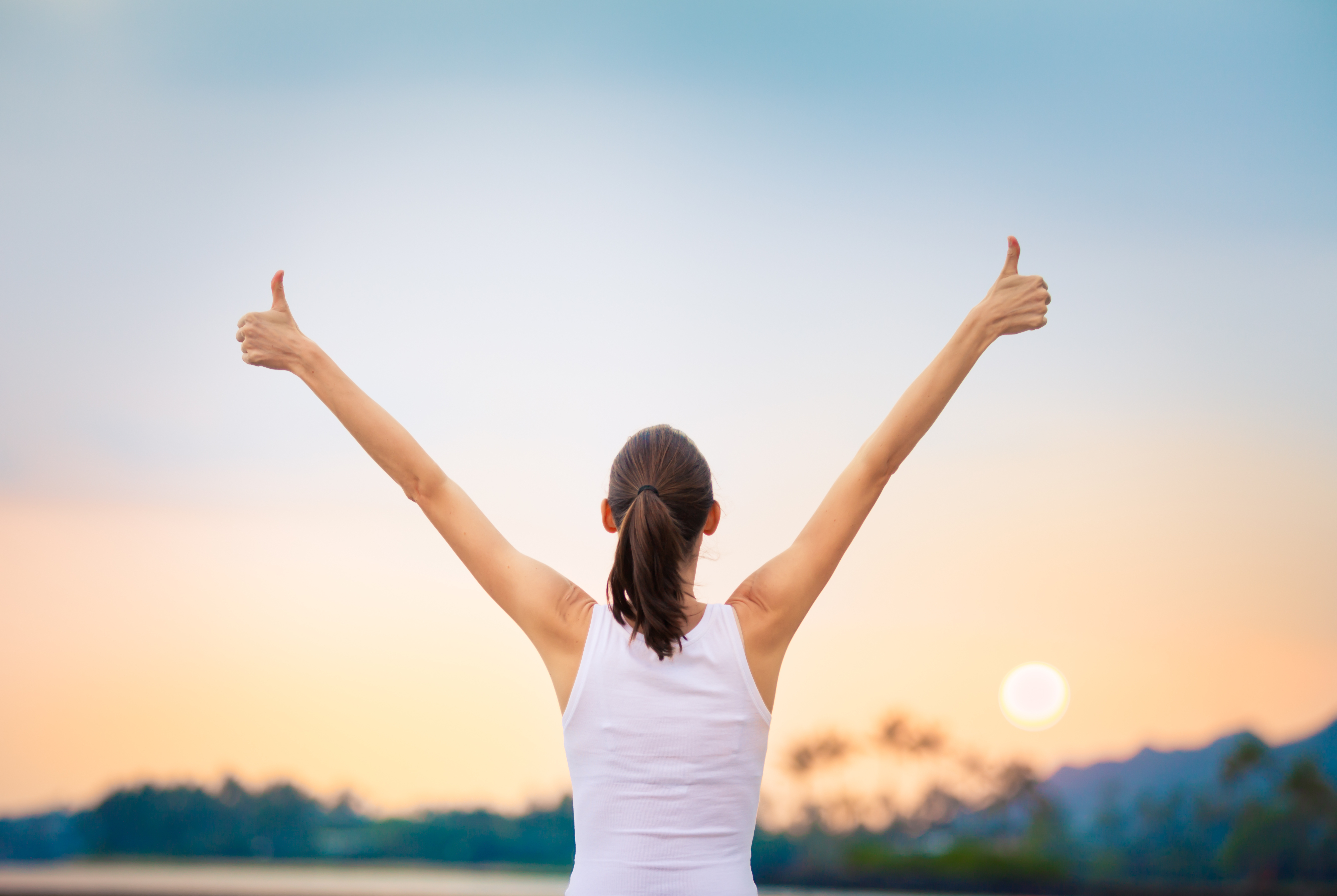 Woman with two thumbs up at sunset