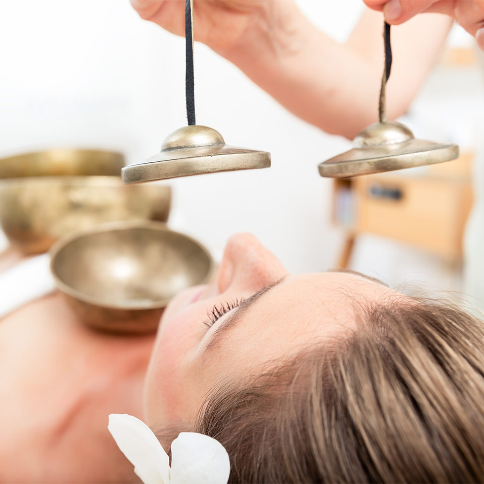 Woman receiving sound therapy - singing bowls lie on her body and a pair of cymbals are held above her head