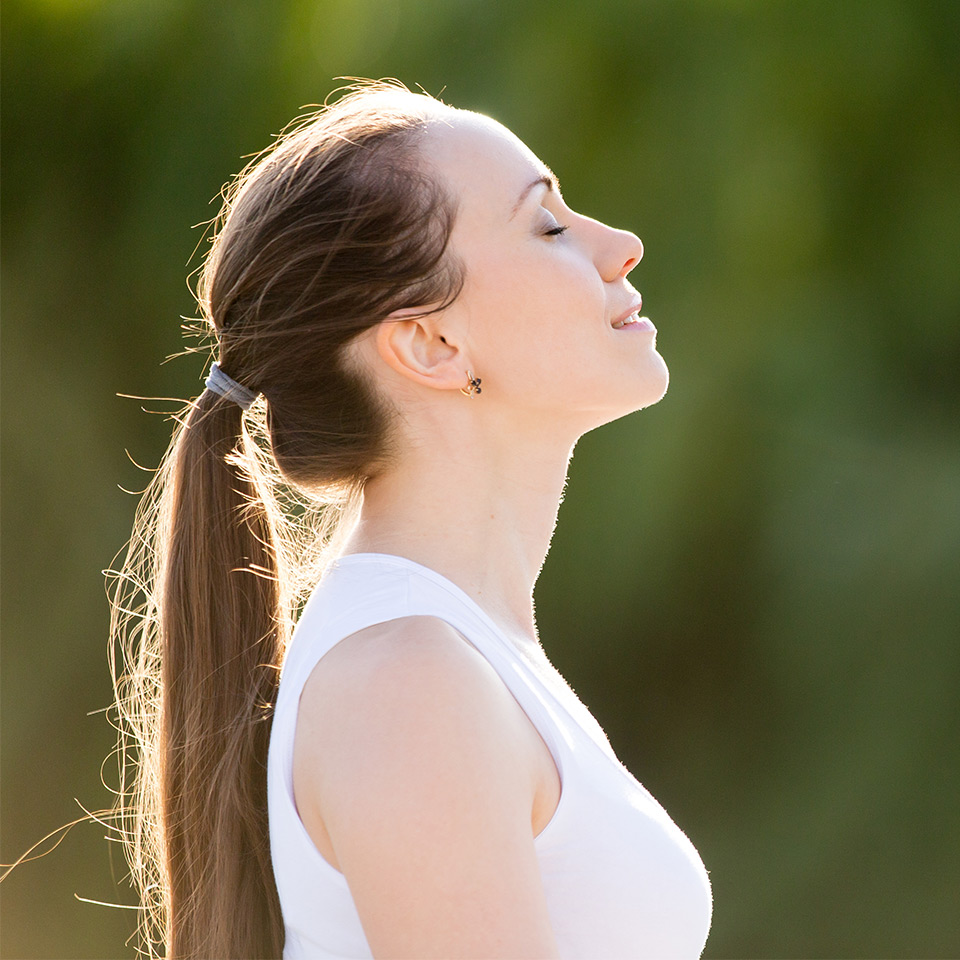 Young woman smiling and looking towards the sky as she stands in front of trees.