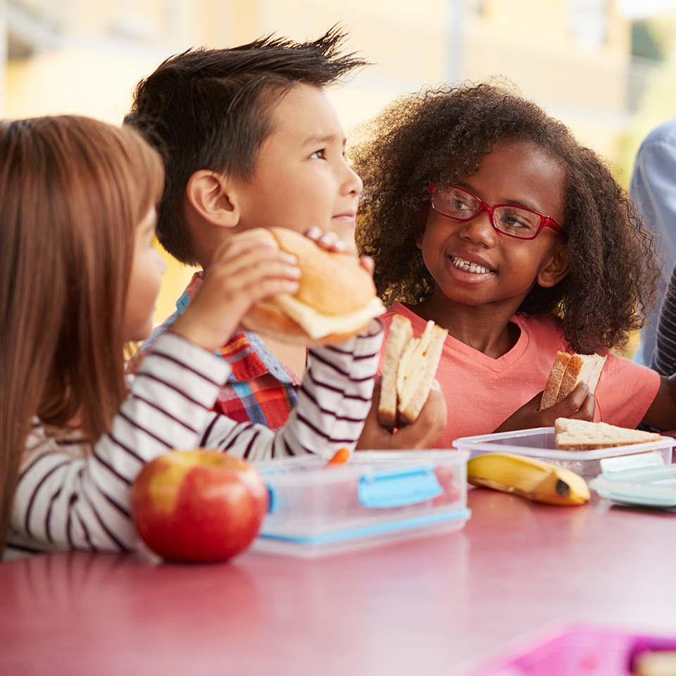 Young school kids eating lunch talking at a table together