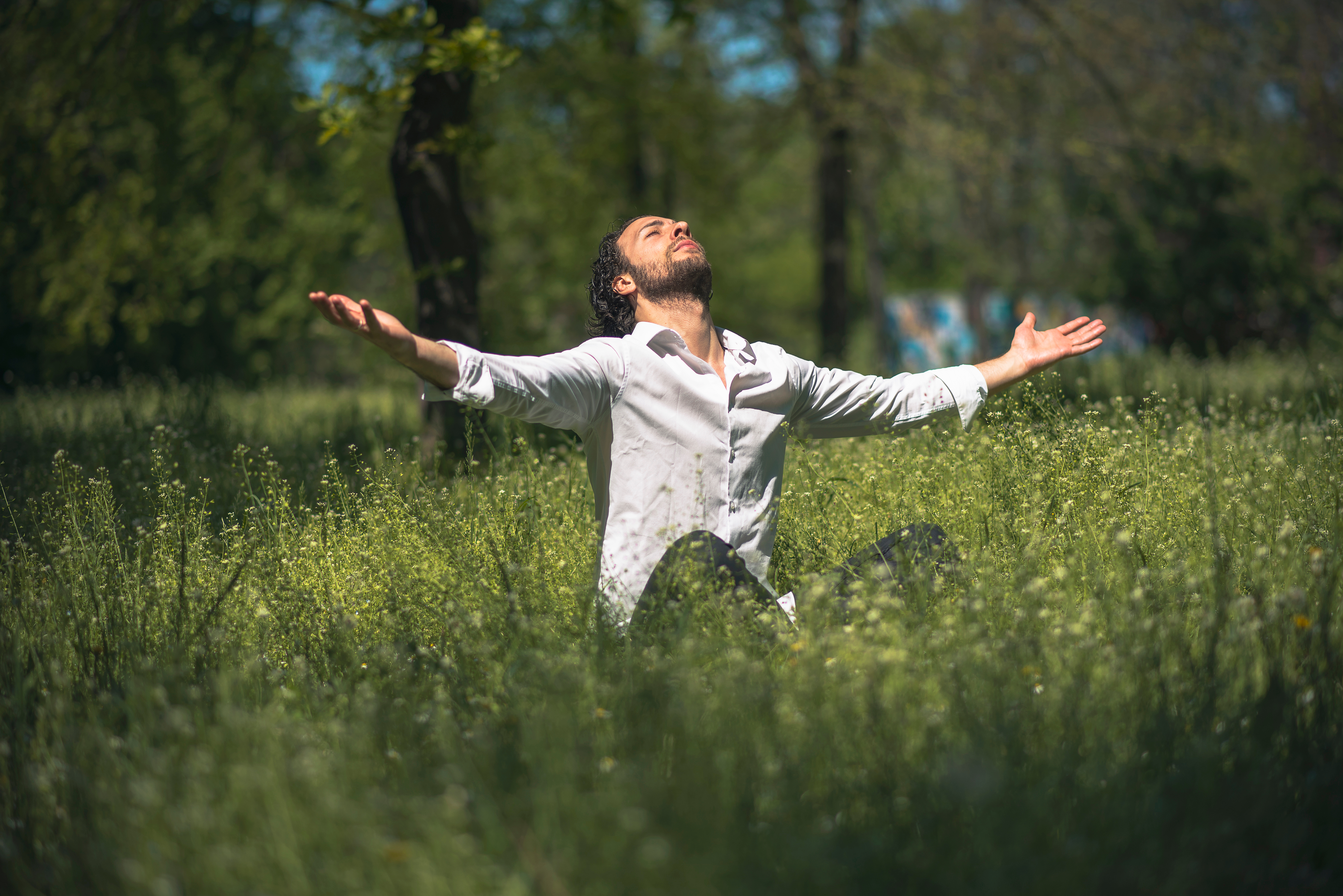 A man in a field, arms out, palms facing upwards, head tilted to the sky