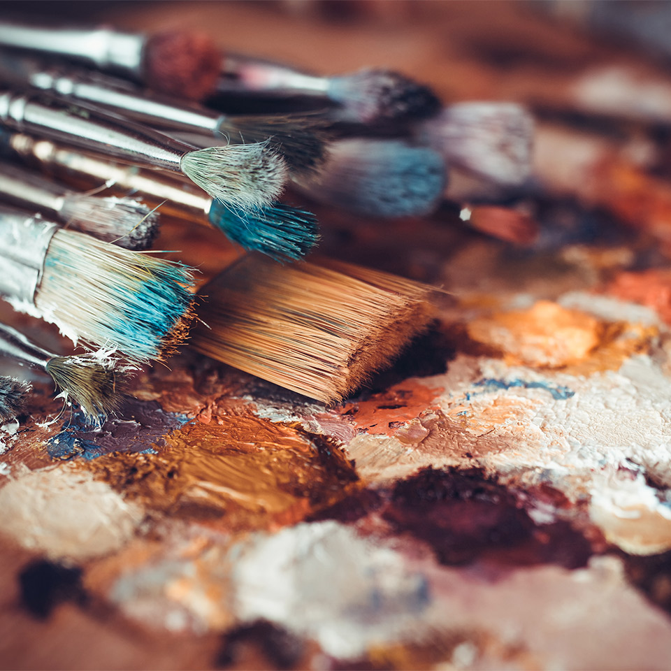 Close-up of paintbrushes, artist palette, and multicoloured paint stains