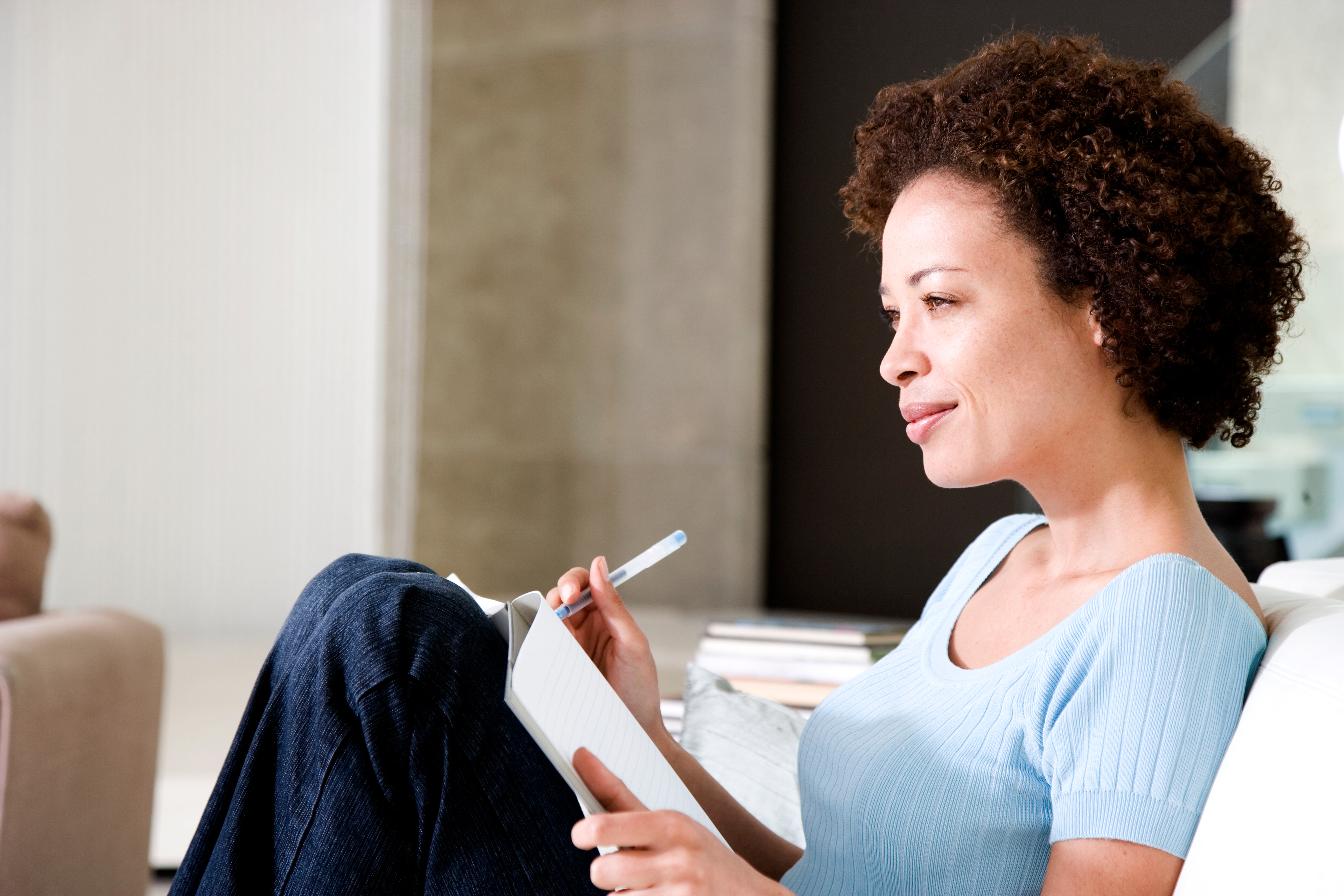 Someone with a journal and pen, looking into the distance and smiling slightly