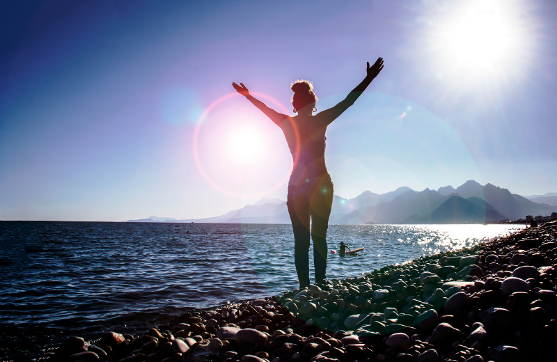 Woman standing at water's edge wioth arms raised