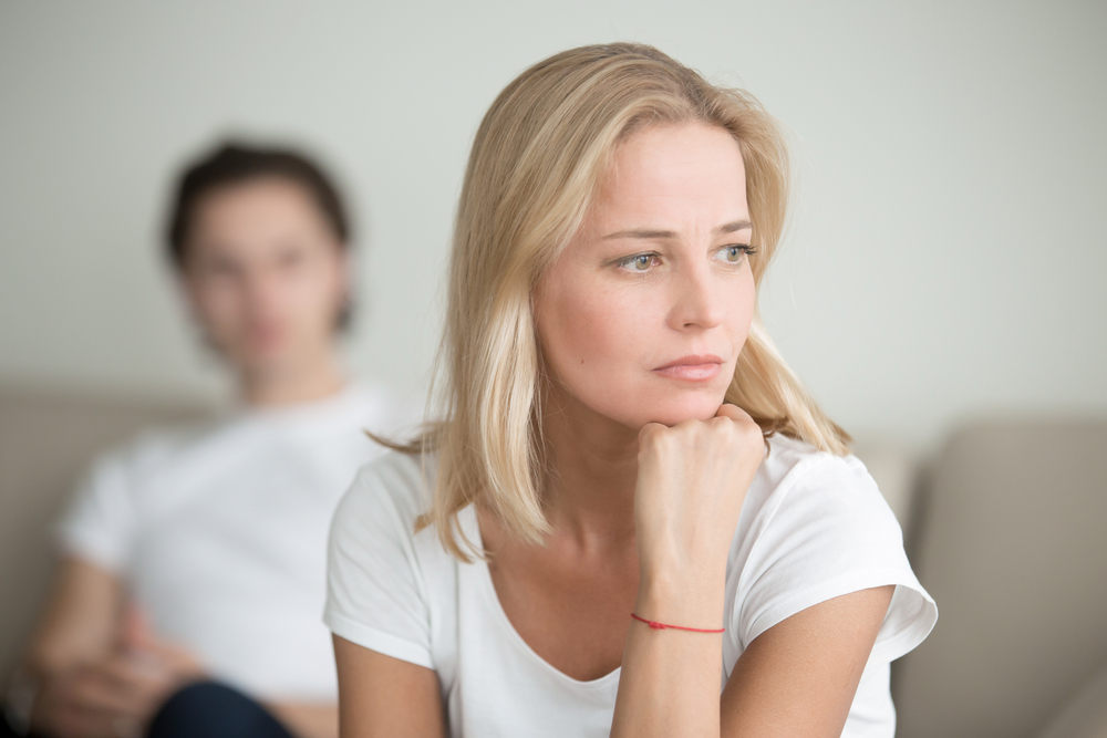 Woman looking sad staring into the distance with her partner blurred out behind her