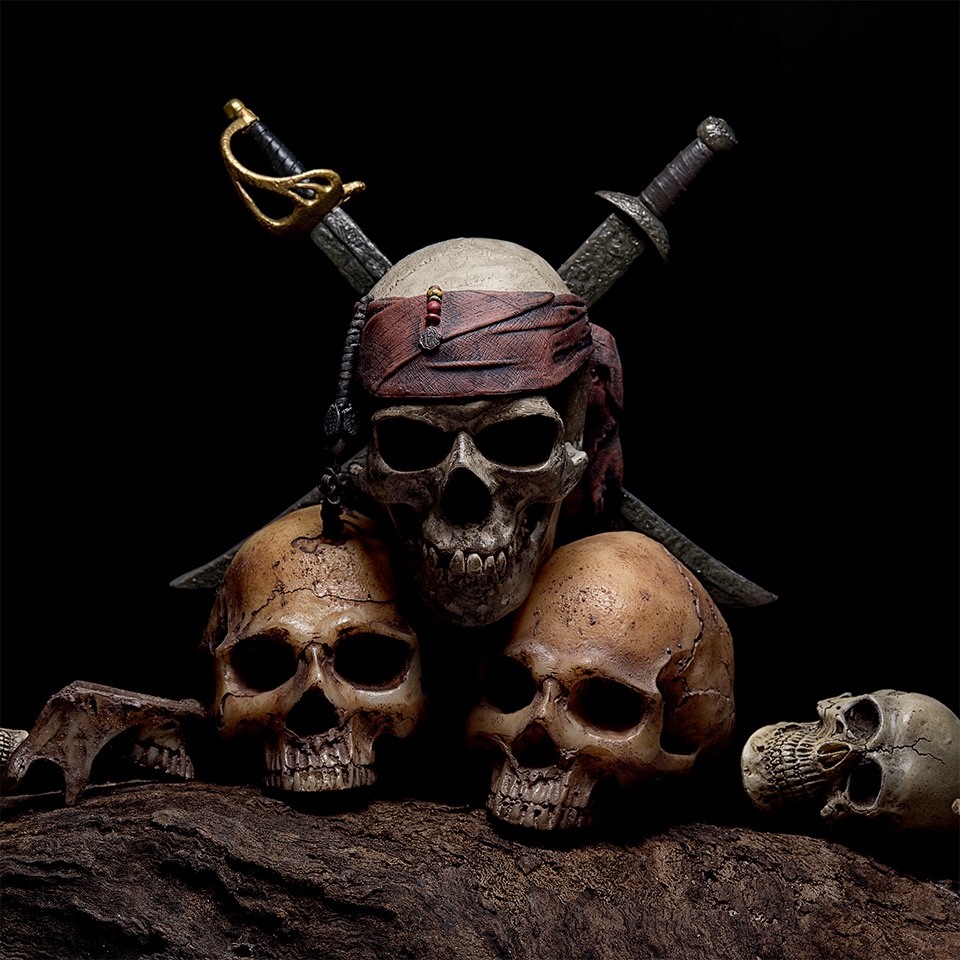 Still life with pirate skull with two swords and four human heads on a dark background.