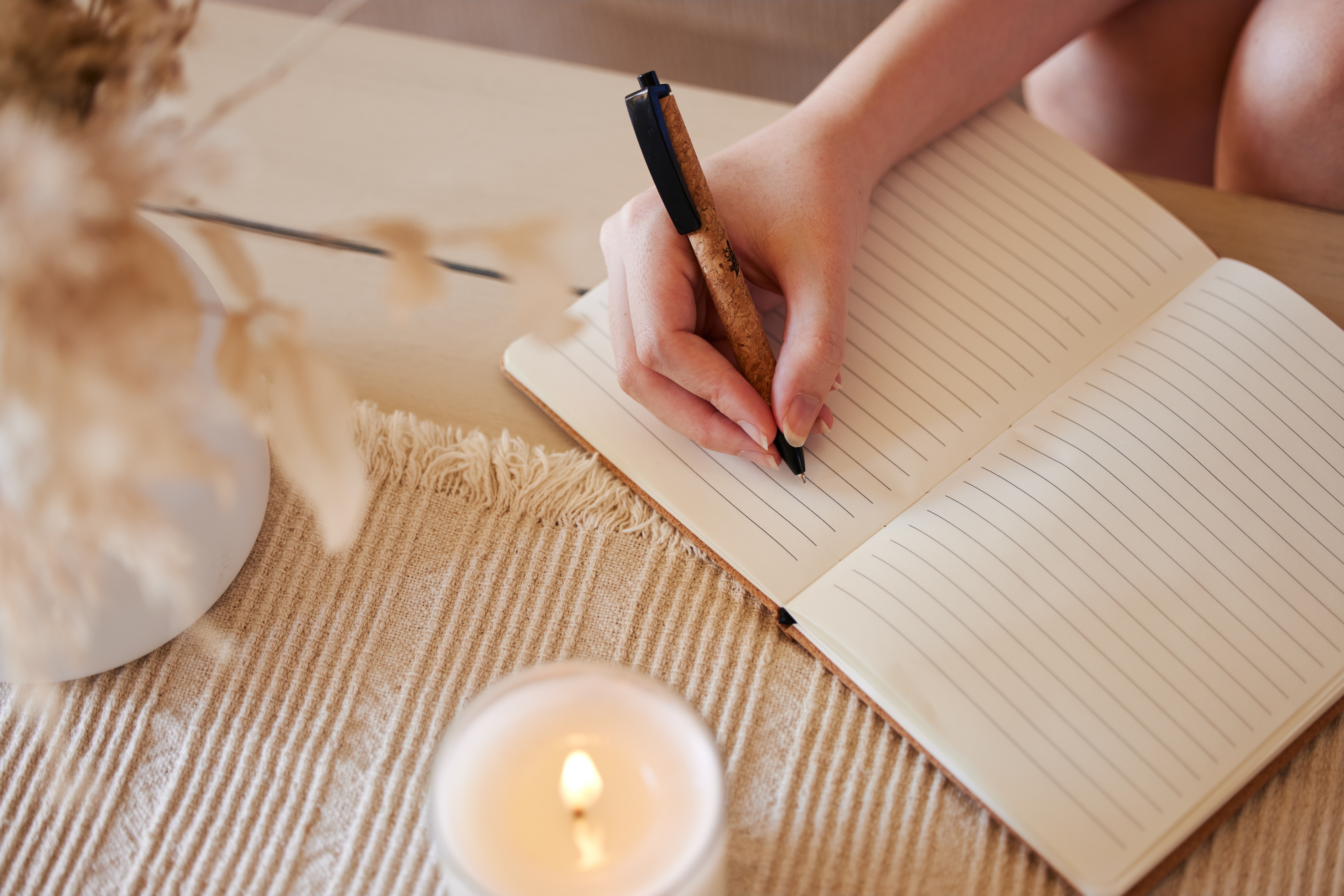 A lit candle next to someone writing in a journal