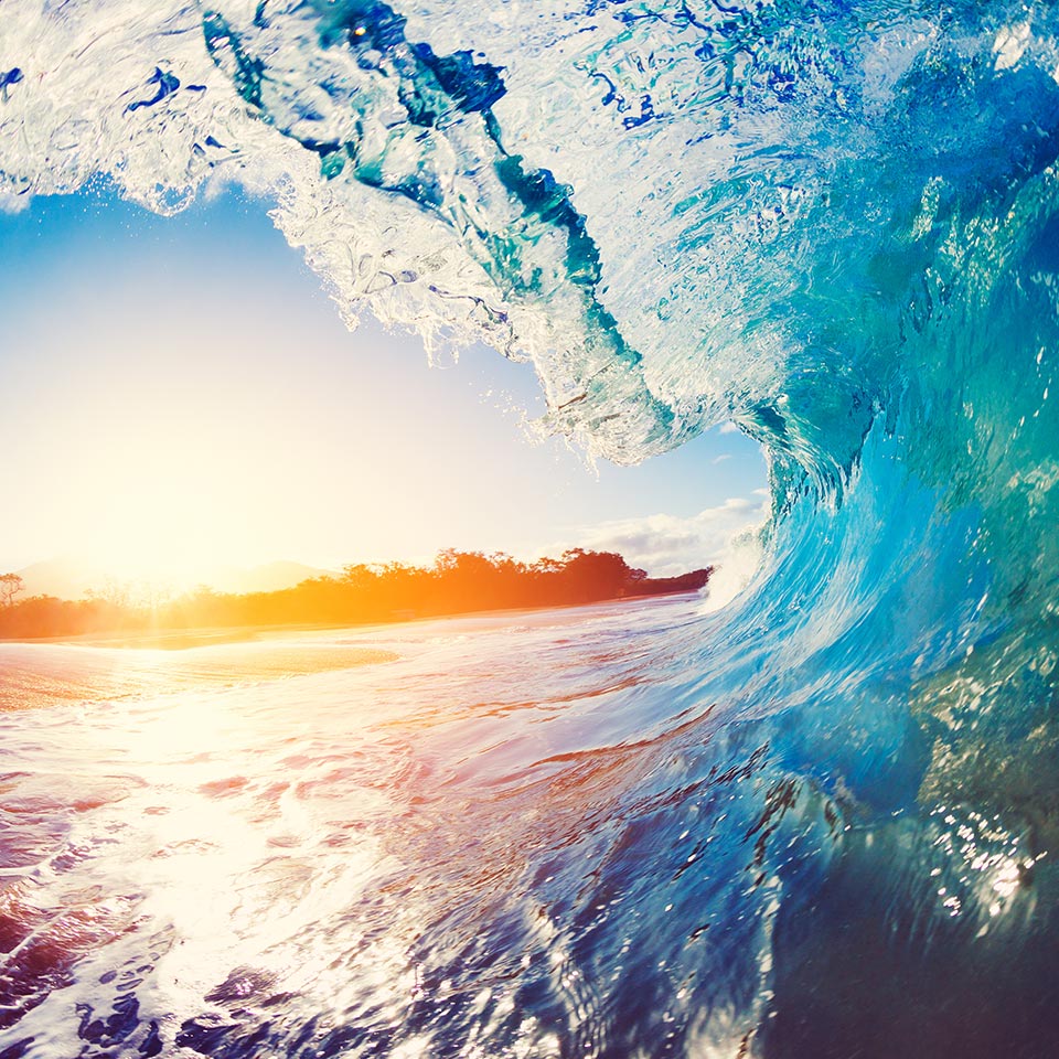 Blue ocean wave crashing at sunrise