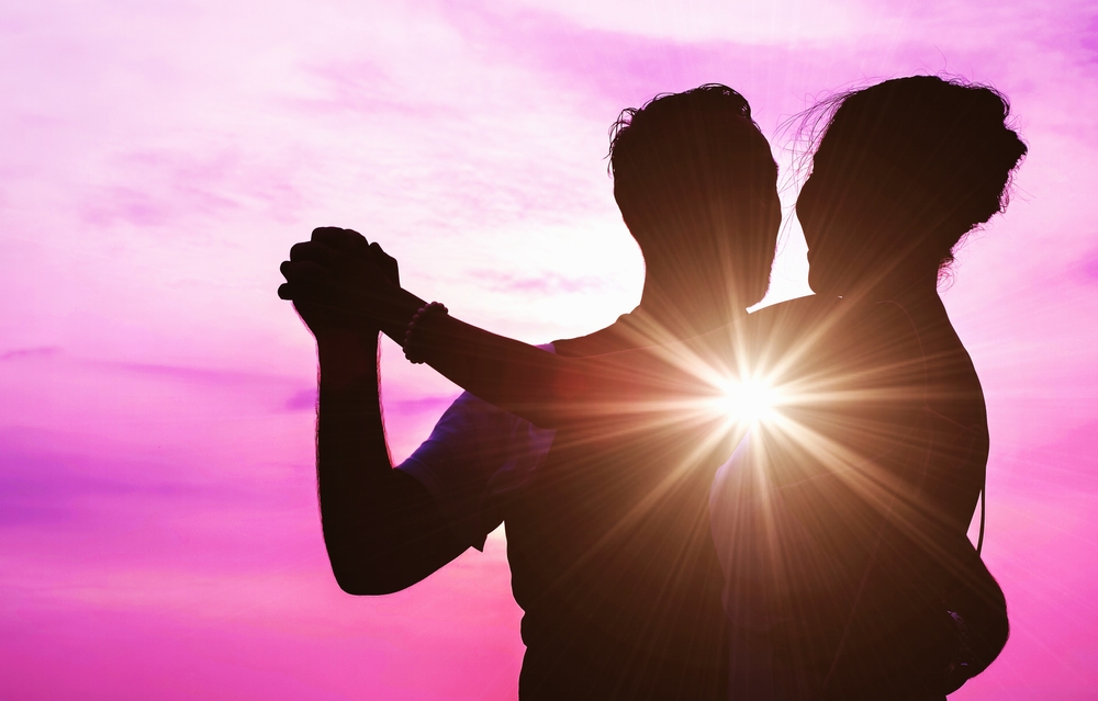 Silhouette of a couple dancing with the sun shining between them and a pink sky behind