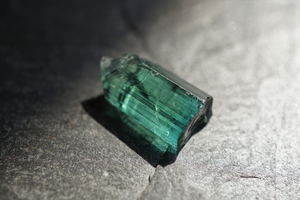 A piece of Green Tourmaline on concrete