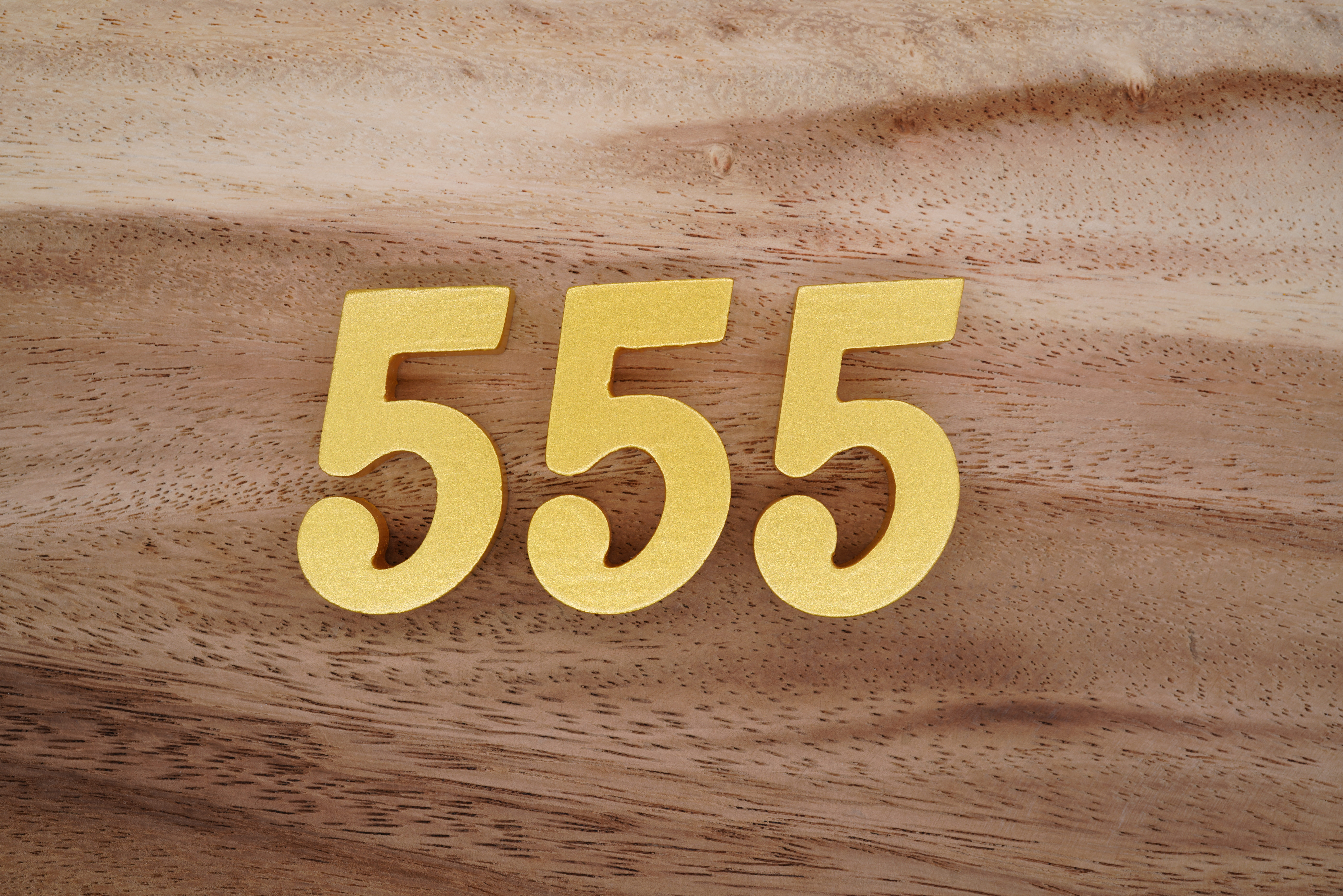 Three gold 5's written on a wooden background