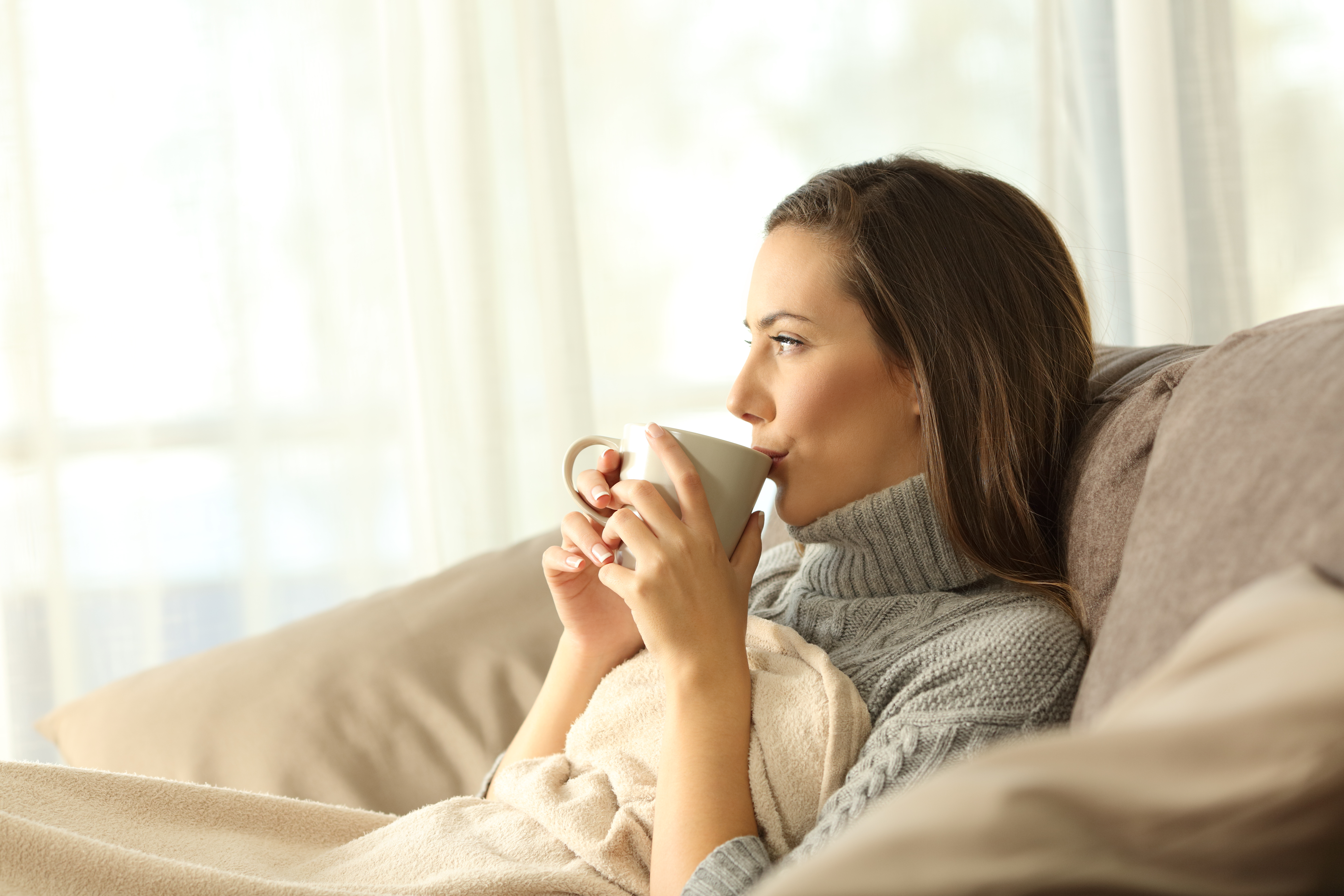 Someone sat on the sofa with a blanket and a hot drink in a mug