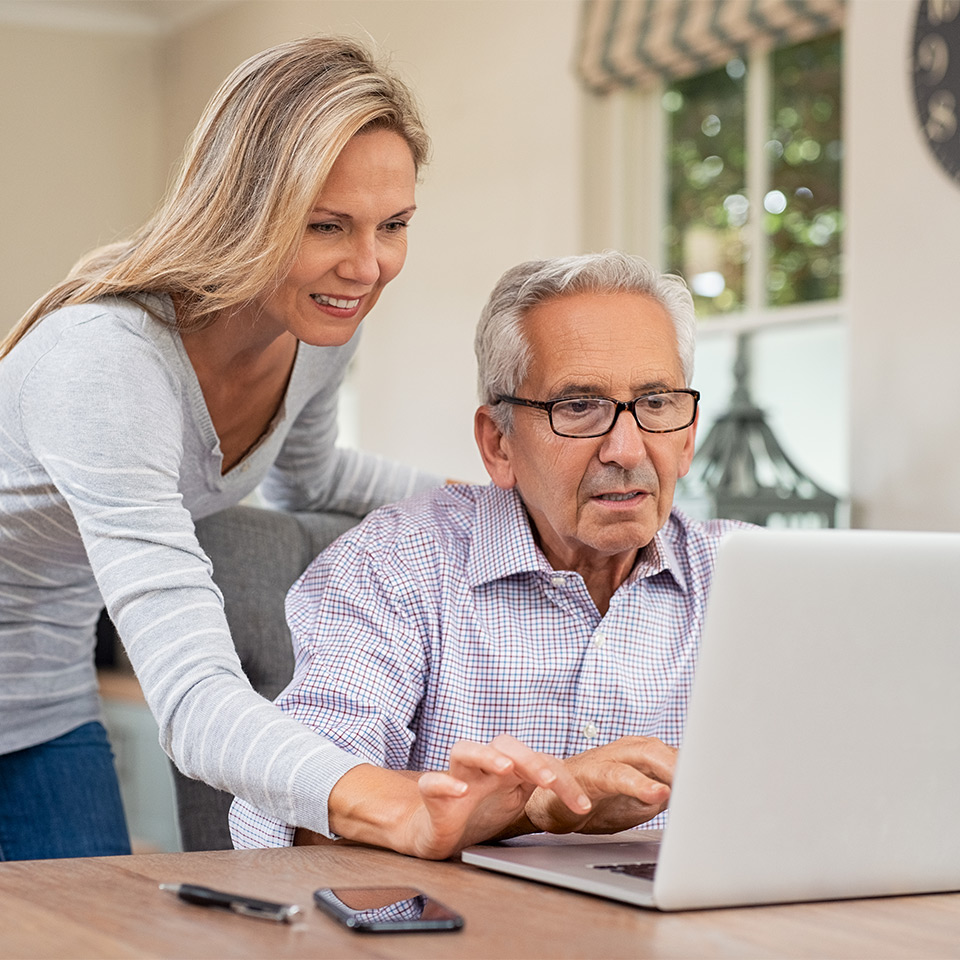 Senior man and mature daughter smiling and looking at a laptop as they learn computer skills