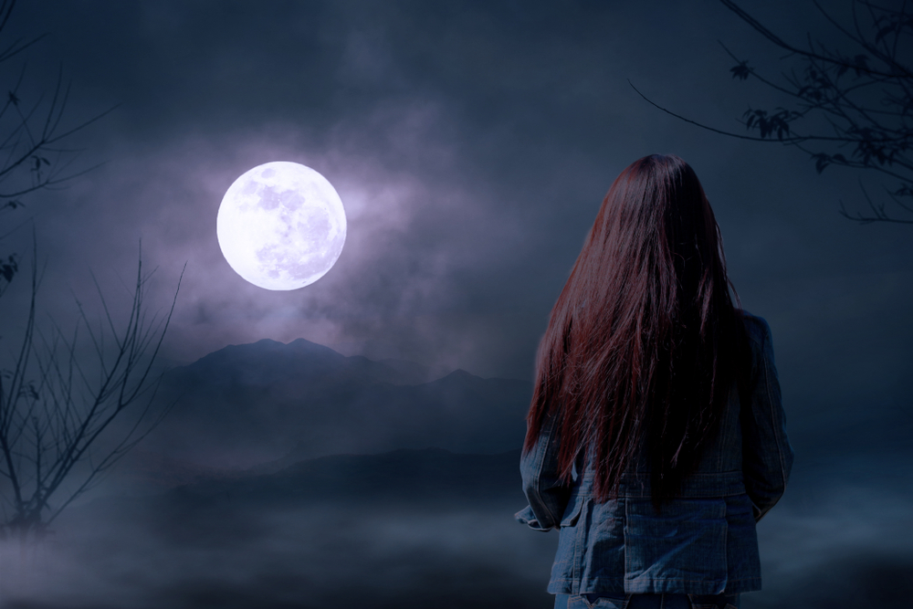 The back of a woman outdoors looking at a full moon