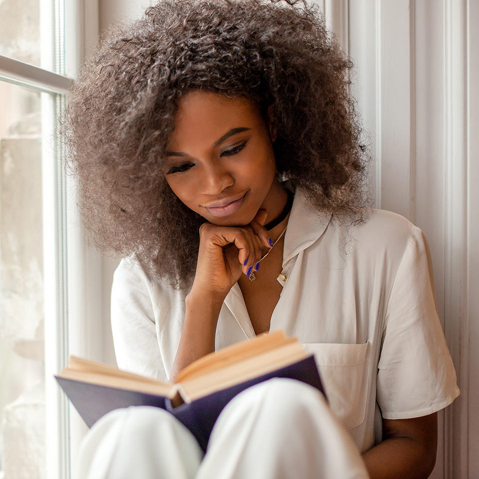 Woman sitting on a windowsill reading a book