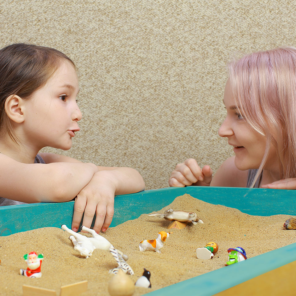 A child in sand tray therapy talking with a therapist