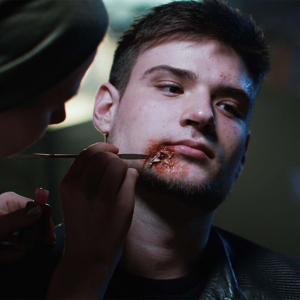 Special FX makeup artist applying blood makeup on the face of a young man